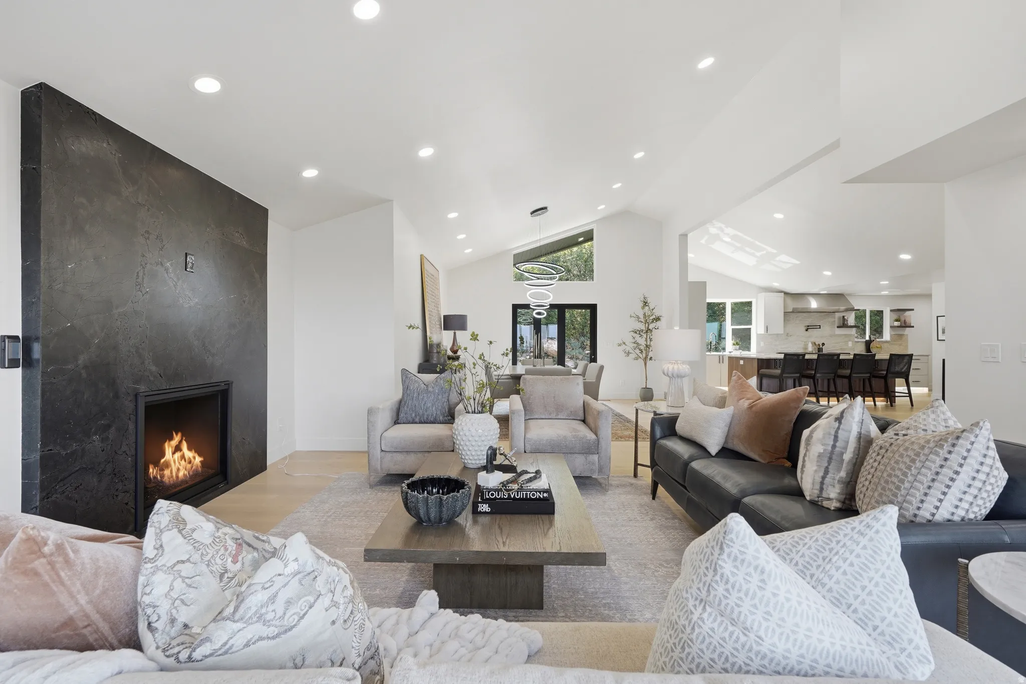 Vaulted ceilings, recessed lighting, wood-finish flooring, and a floor-to-ceiling fireplace with a dark stone-look finish