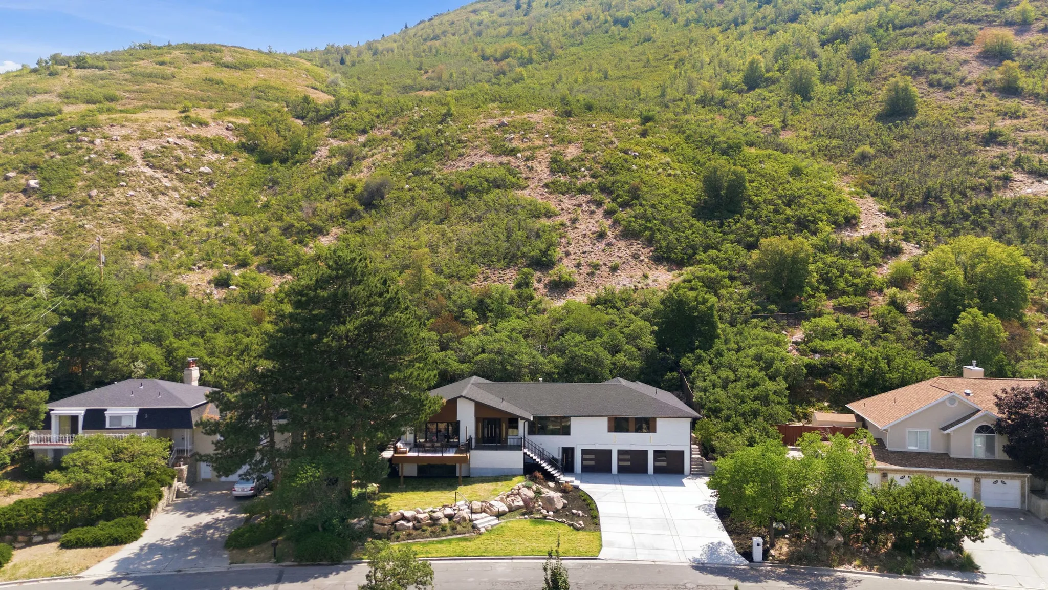 Modern exterior, three-car garage, large driveway, terraced landscaping, mountain backdrop