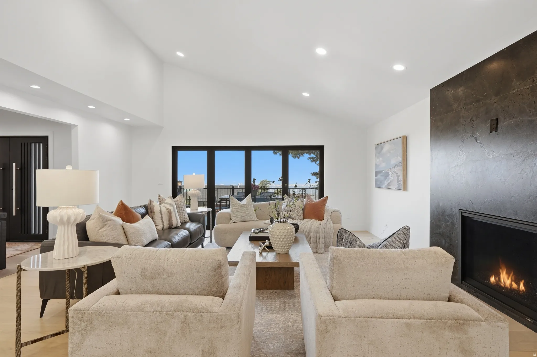 Vaulted ceilings with recessed lighting, floor-to-ceiling fireplace, and expansive glass doors
