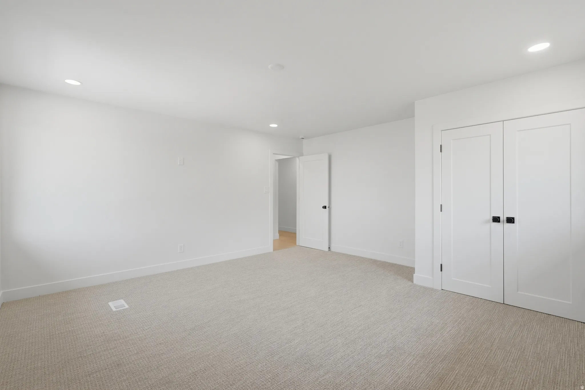 Recessed ceiling lighting, white interior doors with matte black hardware, light-toned carpet flooring, and white painted walls