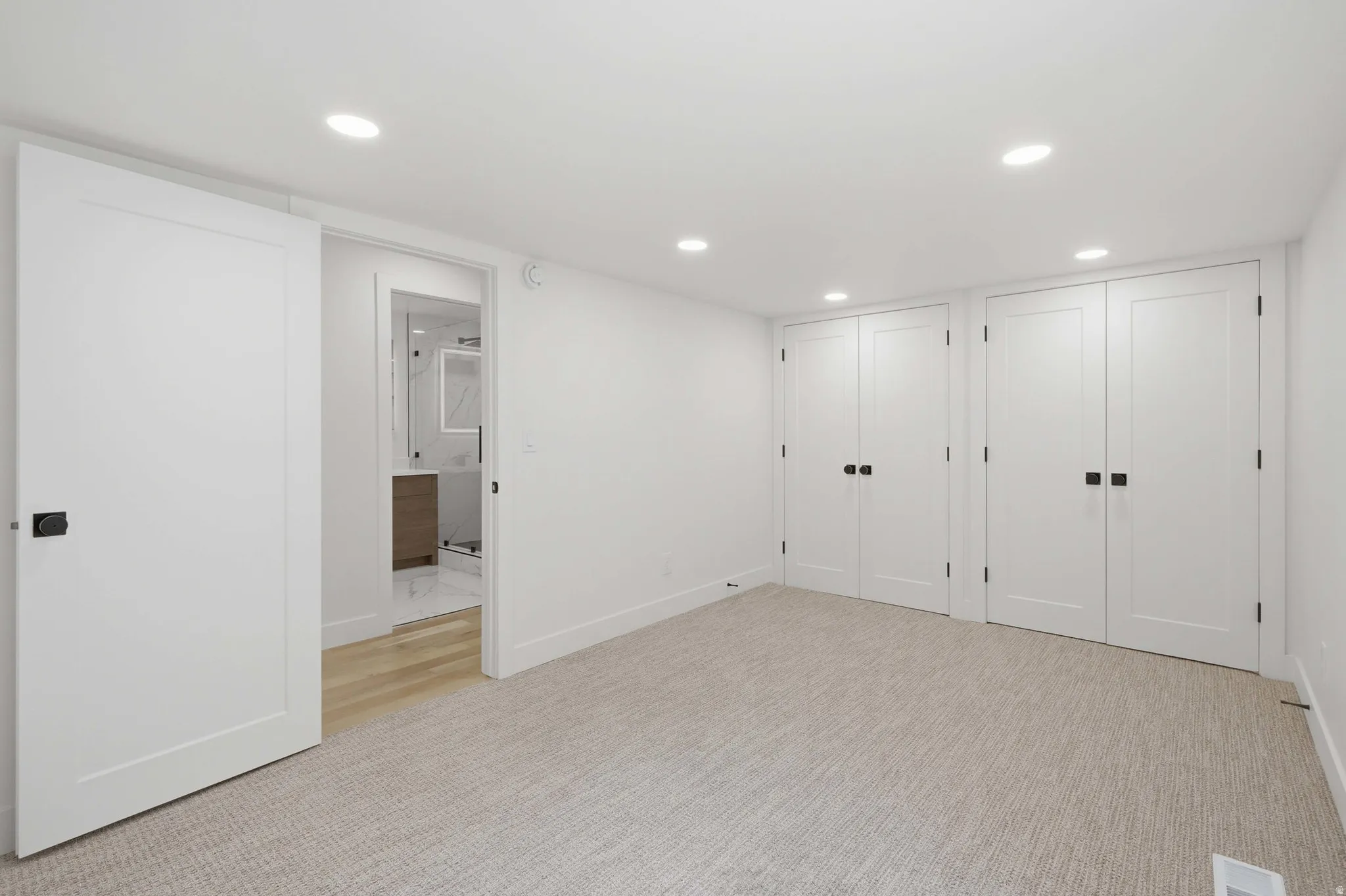 Recessed lighting illuminates the carpeted flooring and four panel doors
