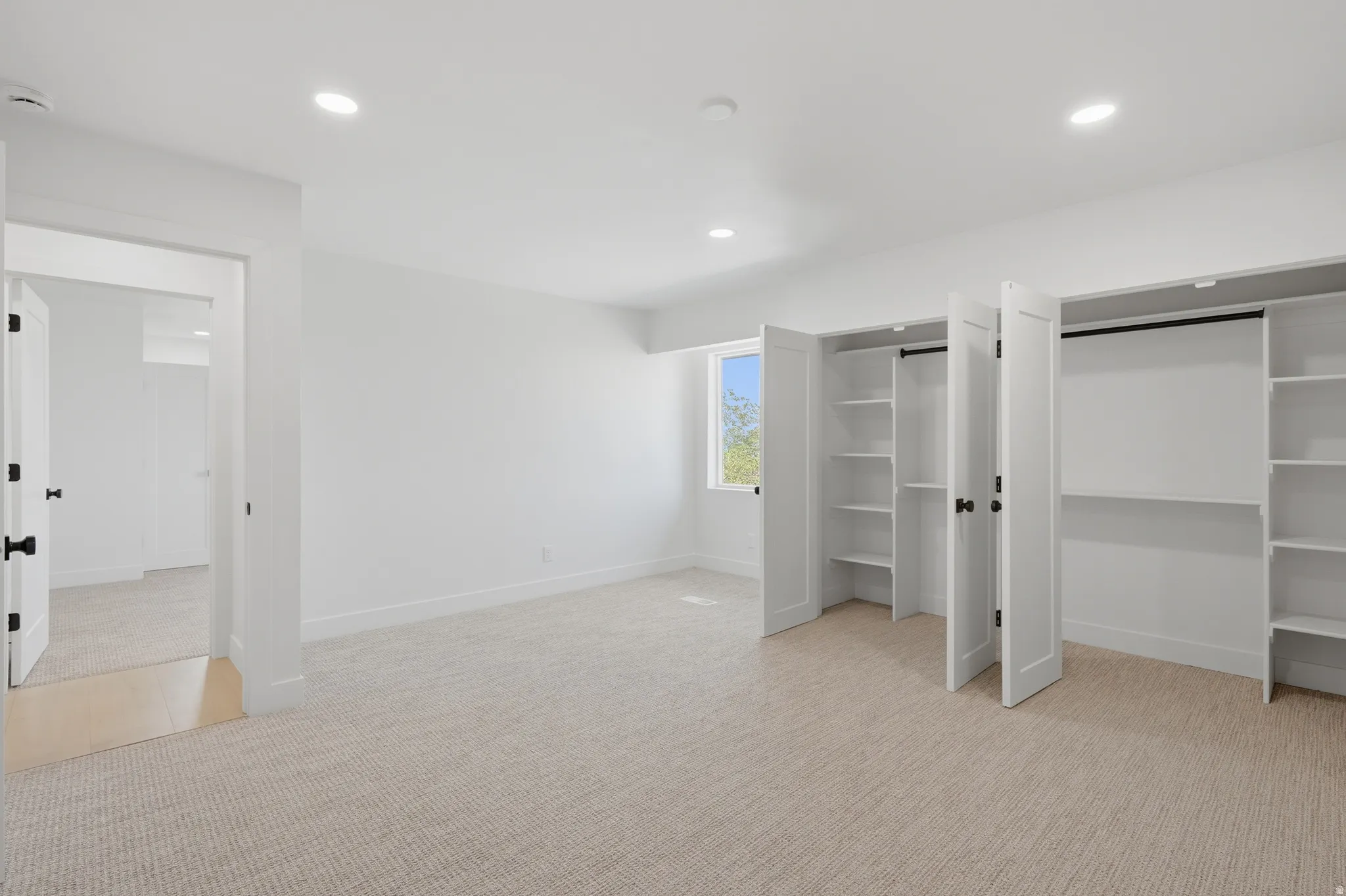 Neutral tone carpeting, built-in closet shelving, white interior doors, recessed lighting, and a single window