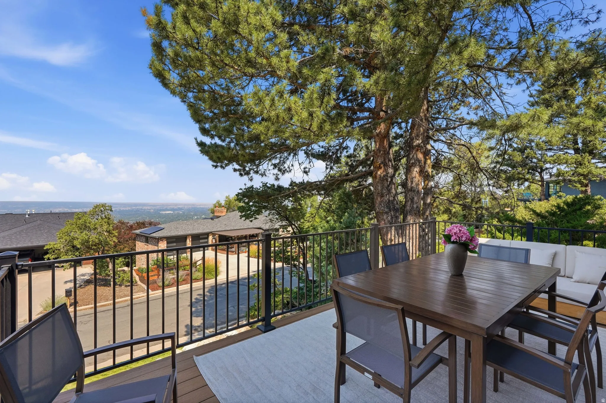 Expansive outdoor deck with wood-finish flooring, black metal railing, and mature evergreen trees providing natural shade