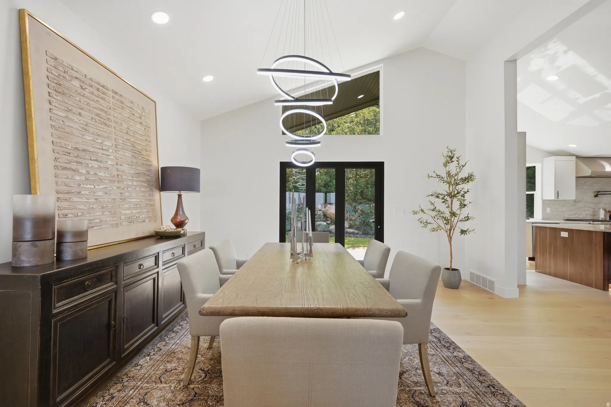 Vaulted ceilings, contemporary pendant lighting, wood-finish flooring, recessed lighting, and black-framed French doors