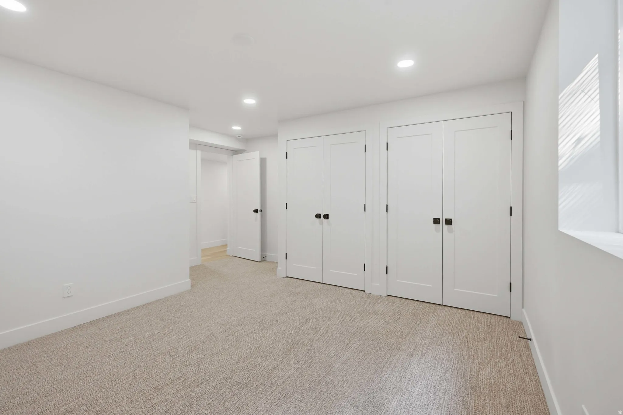 Recessed lighting, light-colored carpeting, white walls, and multiple built-in closets with matte black hardware