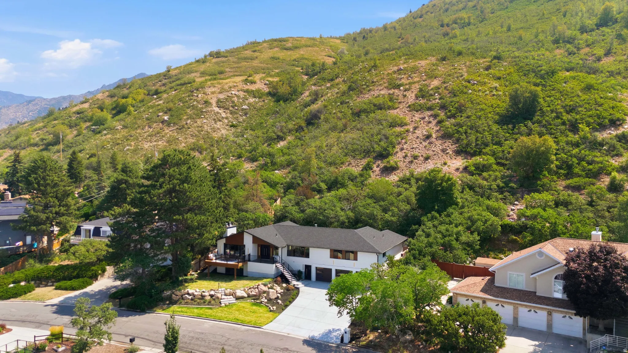 Contemporary residence with a black roof, white exterior, and a prominent hillside backdrop