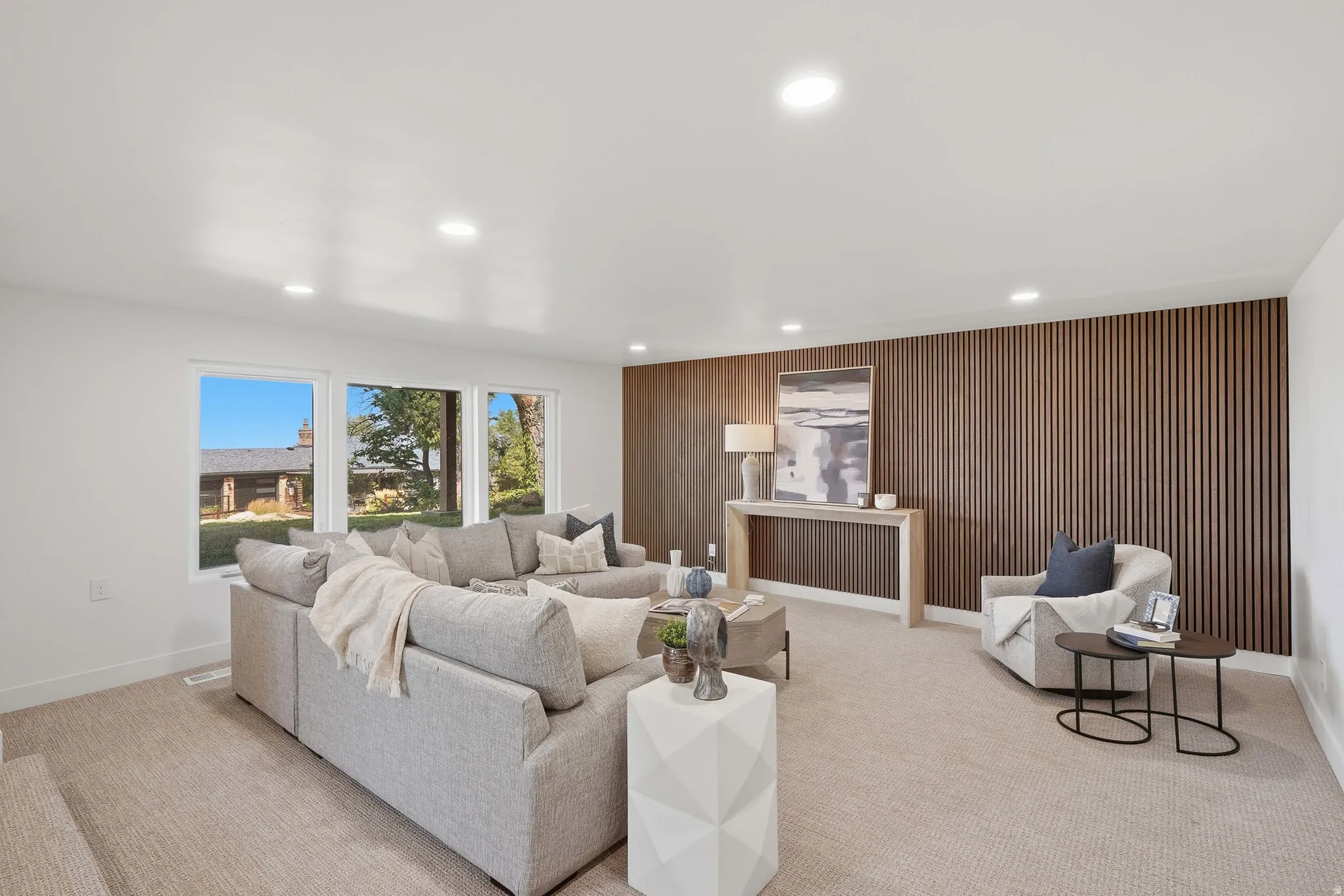Recessed lighting, wood slat accent wall, three large windows, and neutral carpet