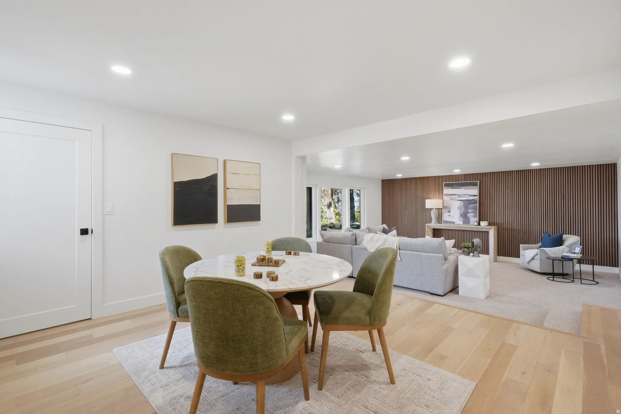 Recessed lighting, light wood-finish flooring, white walls, built-in wood slat accent wall, and a white interior door with black hardware