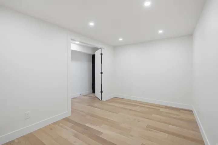 Recessed lighting illuminates the room, featuring light wood-finish flooring and a white paneled door