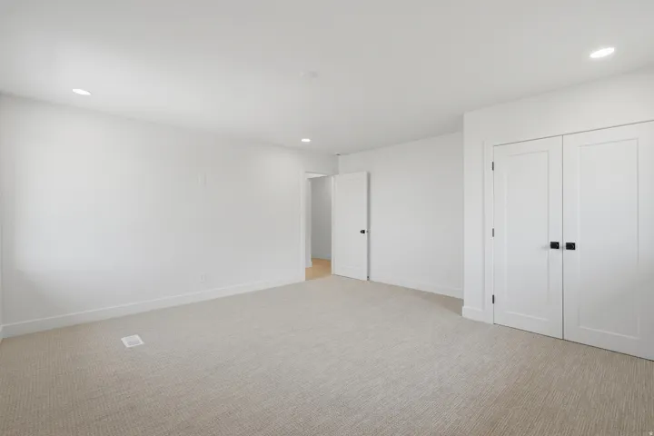 Recessed ceiling lighting, white interior doors with matte black hardware, light-toned carpet flooring, and white painted walls