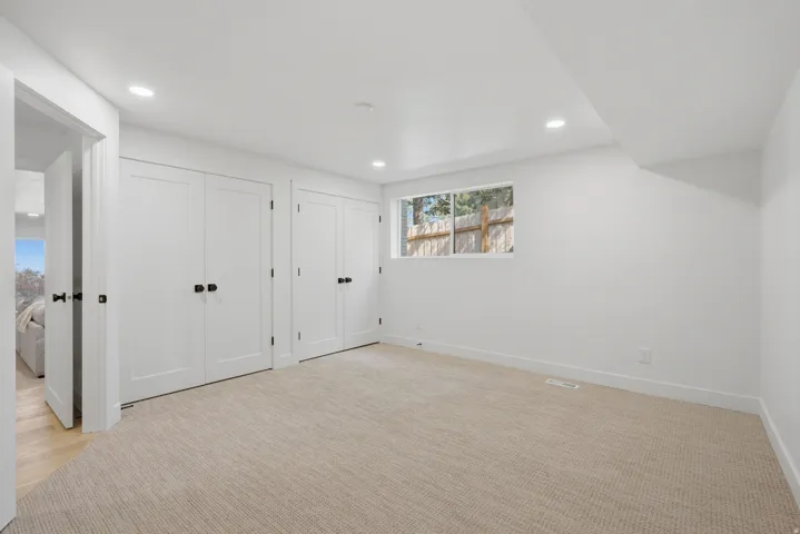 Recessed lighting, light-toned carpeting, white walls, and a window with a wooden fence background