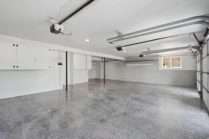 Expansive garage with epoxy flooring, white built-in cabinetry, and integrated overhead lighting
