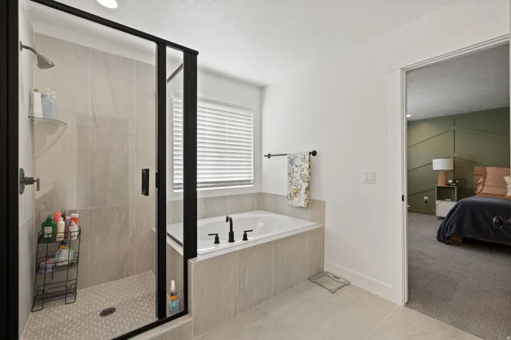 Walk-in shower with black-framed glass enclosure, built-in tub with black fixtures, and light-toned tile flooring