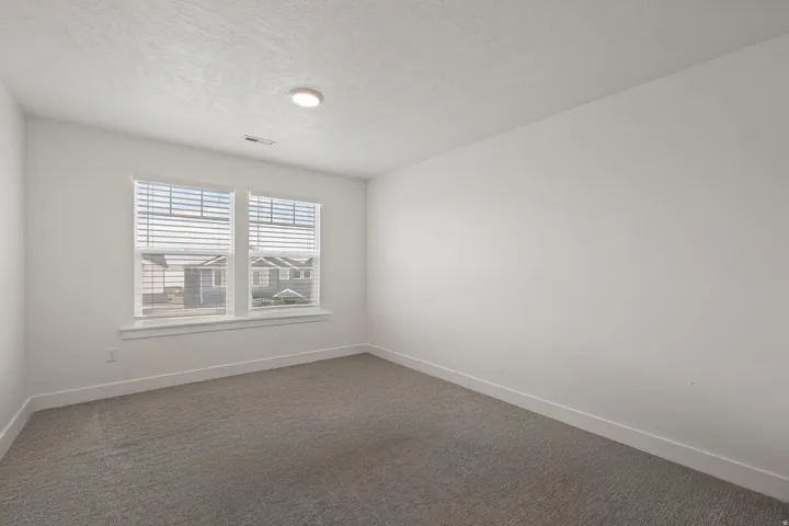 Light gray carpet flooring, white painted walls, two windows with blinds, and a flush-mount ceiling light