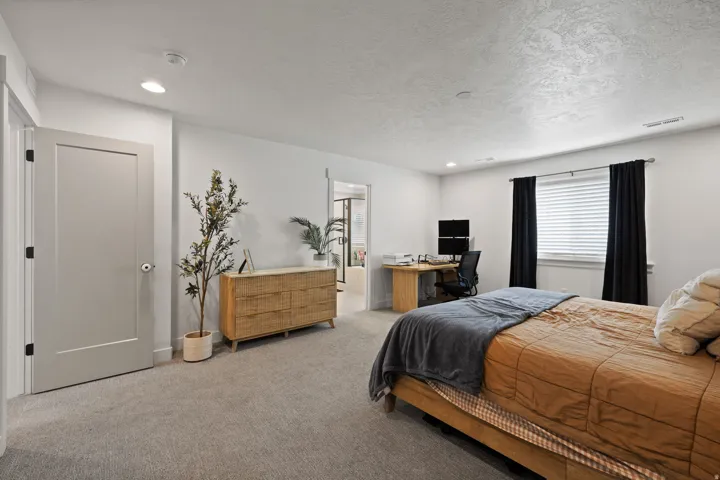 Spacious primary bedroom suite featuring hardwood-finish flooring, abundant natural light from large windows with black drapery, and an ensuite bathroom visible through the doorway