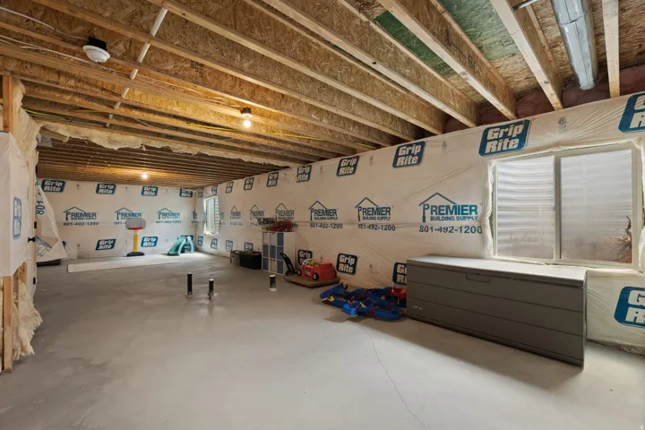 Unfinished basement with exposed ceiling joists, concrete flooring, and multiple windows