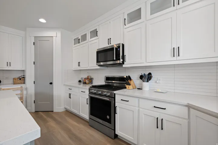 White shaker cabinetry featuring matte black hardware, stainless steel appliances, and a horizontal tile backsplash
