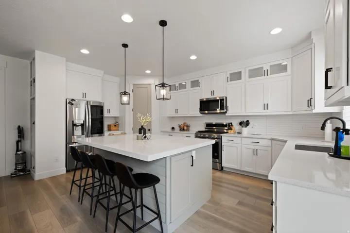 Spacious kitchen featuring an island with seating, white cabinetry, integrated stainless steel appliances, light-toned wood-finish flooring, and pendant lighting