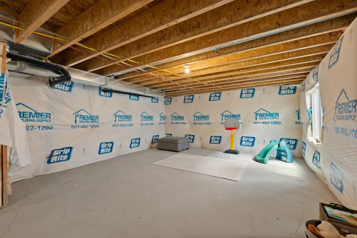 Unfinished basement with exposed wood joists, concrete flooring, and a single window