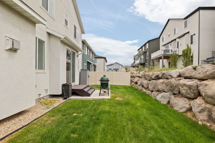 Rear exterior featuring a stone retaining wall, level lawn, and a light-colored privacy fence