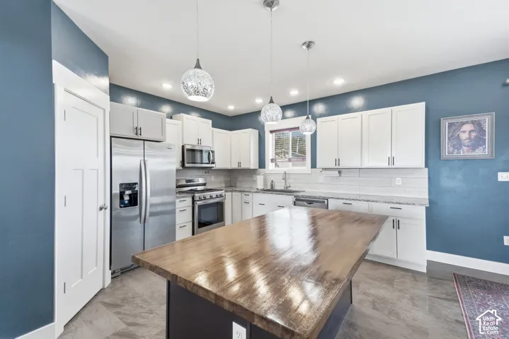Kitchen with a wood-finish island, stainless steel appliances, white cabinetry, and recessed lighting