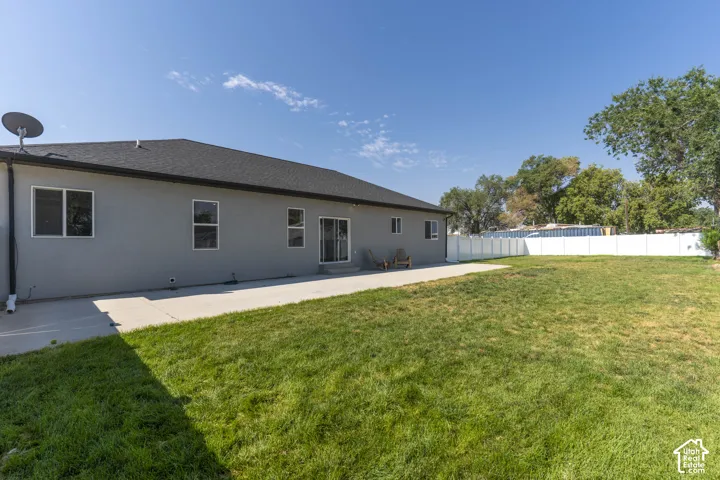 Expansive lawn area with a concrete patio, white privacy fencing, and mature trees
