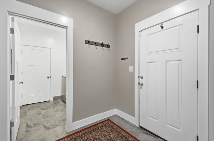 White paneled entry door with chrome hardware, neutral wall paint, and a wall-mounted coat rack
