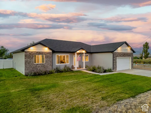 Single-story residence featuring a gray exterior with stone accents, an attached garage, and a lush green lawn