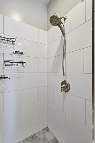 Shower with white subway tile walls, a brushed nickel shower head, and a tile floor