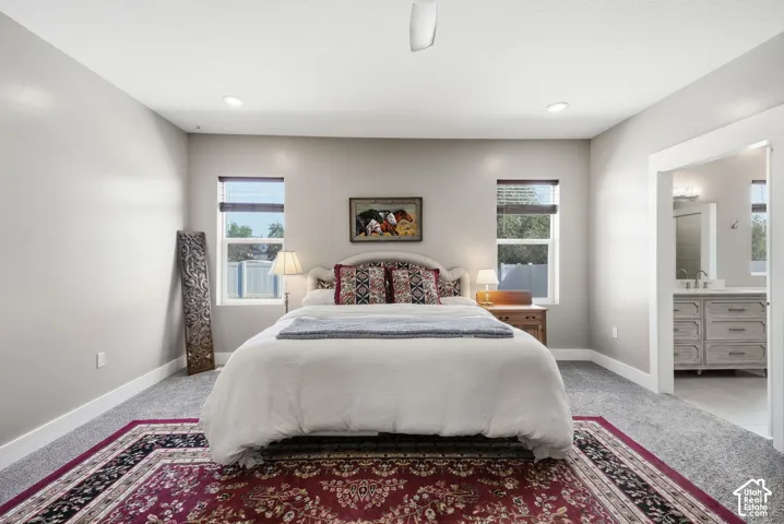 Recessed ceiling lighting, two windows, carpet flooring, and a bathroom entry with a vanity featuring a vessel sink and overhead lighting