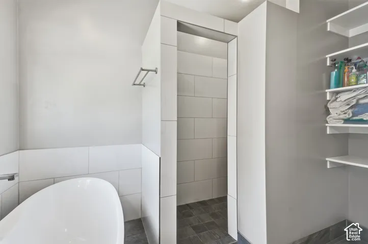 Freestanding soaking tub, tiled accent wall, walk-in shower with tiled surround, and built-in shelving