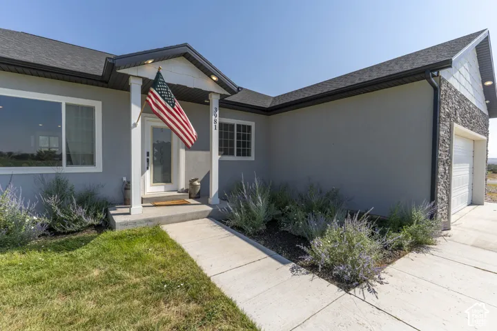 Concrete pathway leading to a covered entry with white pillars, a textured gray stucco facade, and an attached garage featuring stone veneer siding