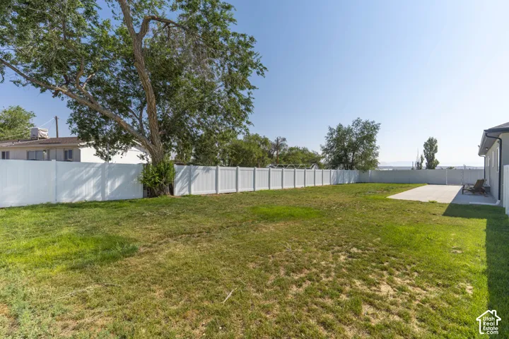 Expansive backyard with a large grass area, mature trees, white privacy fencing, and a concrete patio