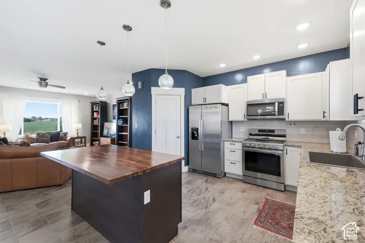 Kitchen featuring stainless steel appliances, white cabinetry, granite countertops, and a wood-finish island