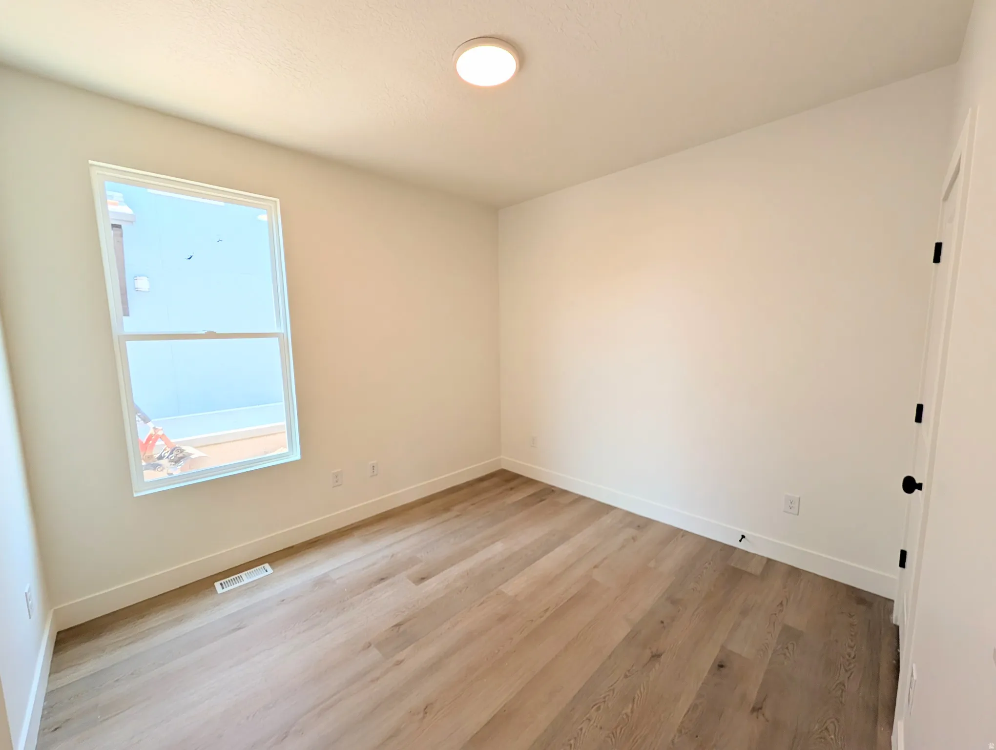Main level bedroom or Office/ featuring a large picture window with natural light, wood-finish flooring throughout, recessed ceiling lighting, and clean white walls with electrical outlets