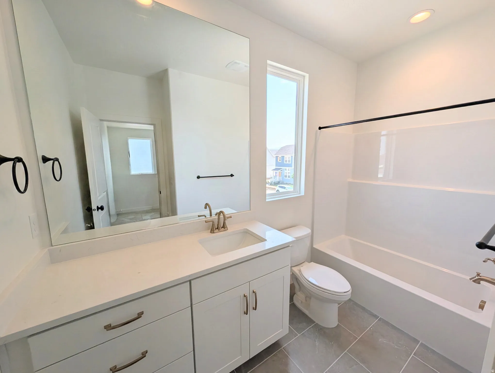 White vanity with brushed nickel hardware, expansive vanity mirror, white subway tile shower surround, and gray tile flooring