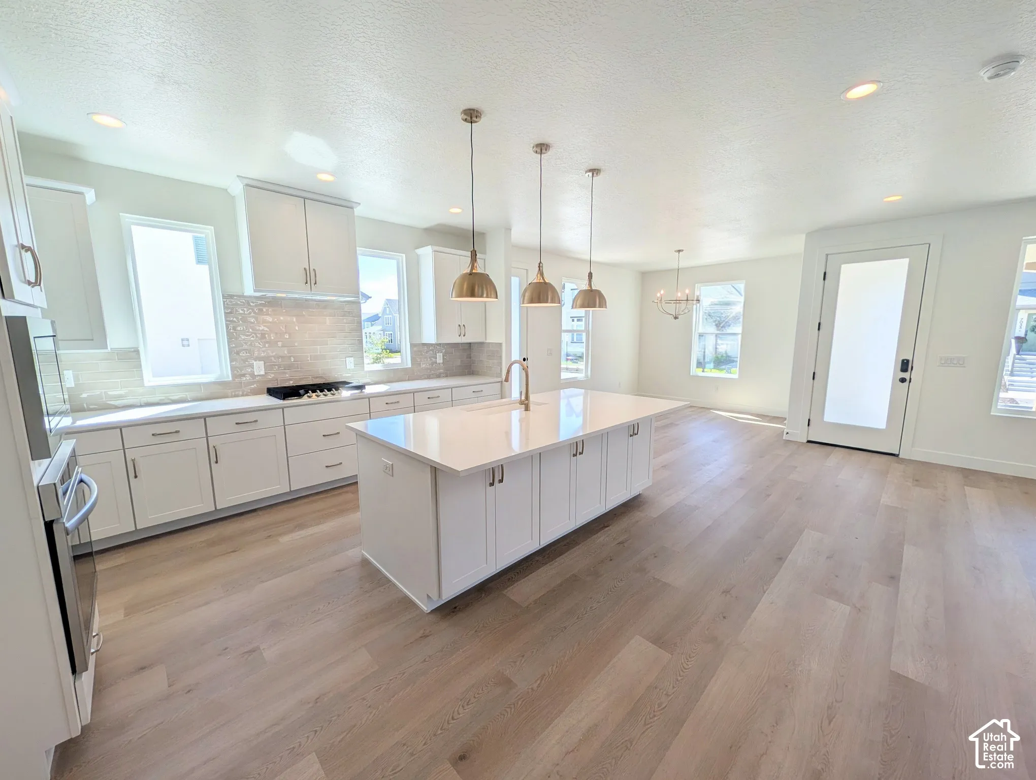 Open-concept kitchen featuring an expansive island with a white countertop, light-toned wood-finish flooring, white cabinetry, and stainless steel appliances