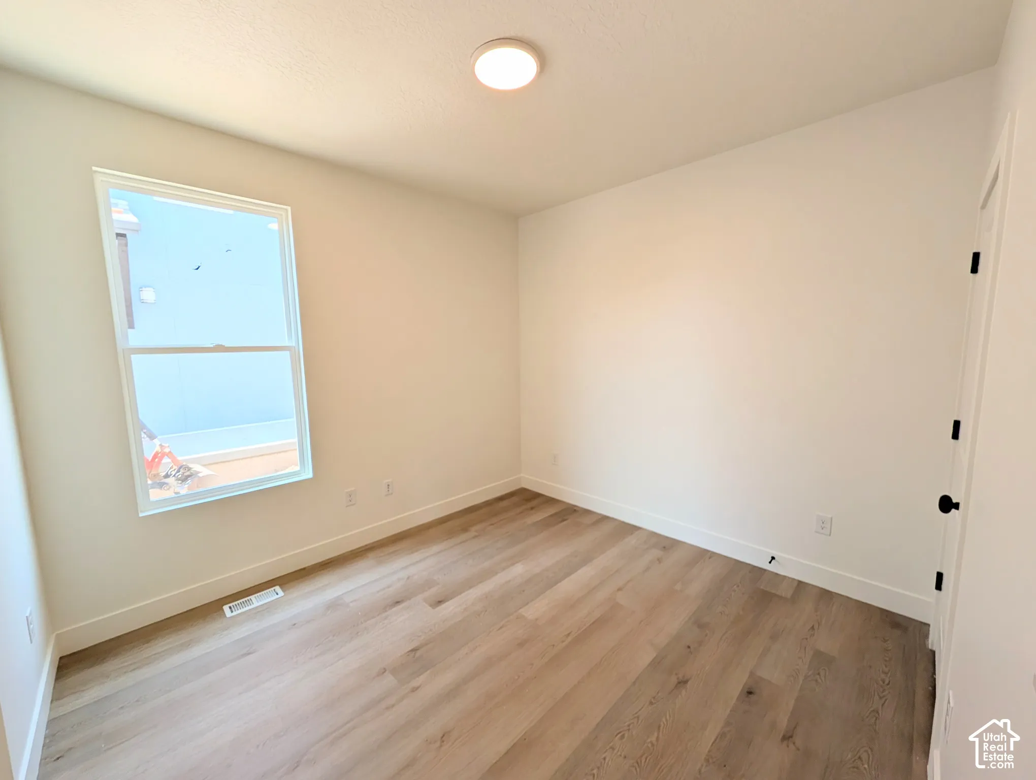 Main level bedroom or Office/ featuring a large picture window with natural light, wood-finish flooring throughout, recessed ceiling lighting, and clean white walls with electrical outlets