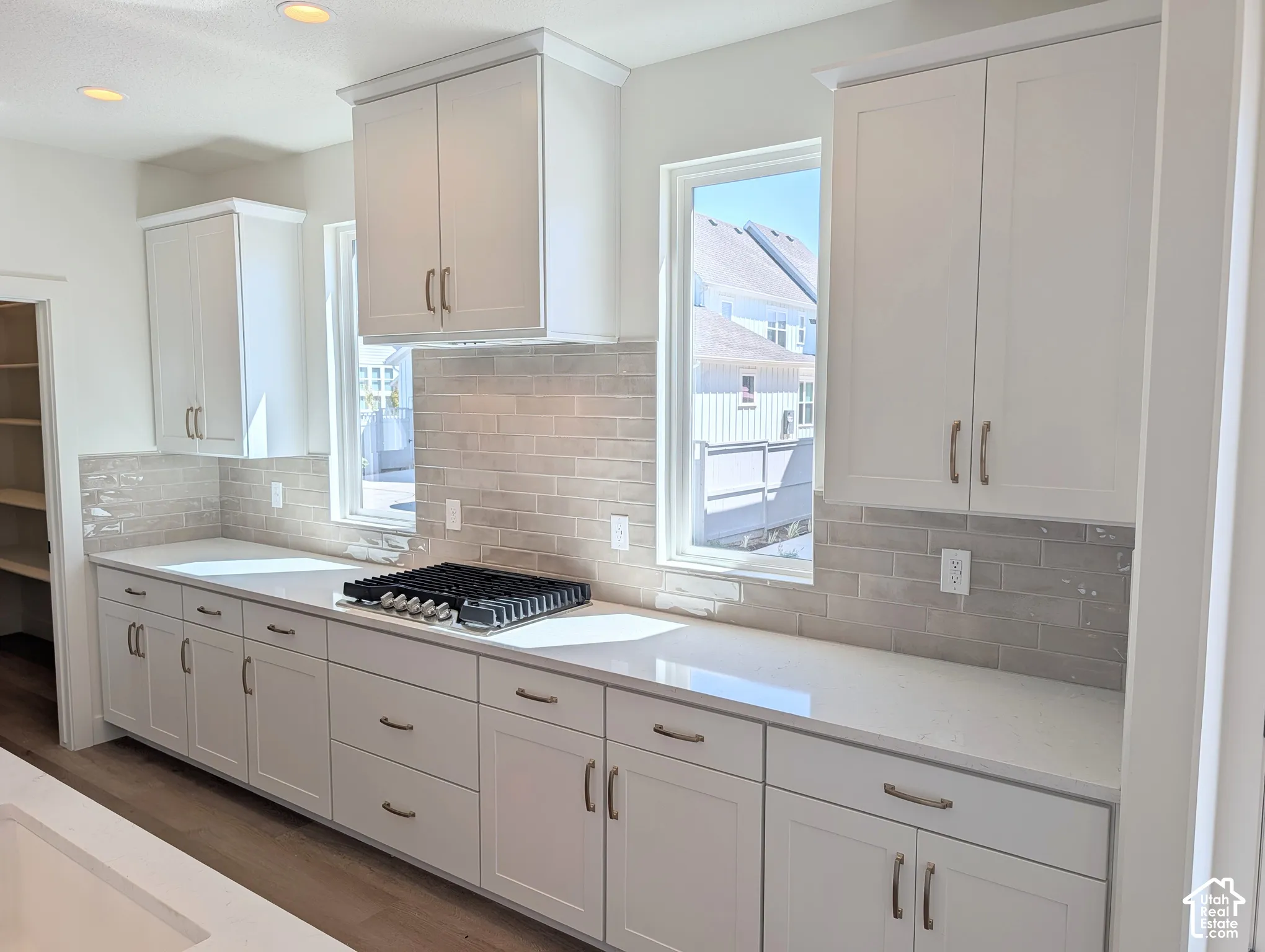White cabinetry with brushed nickel hardware, light-toned countertops, subway tile backsplash, gas cooktop, and recessed lighting