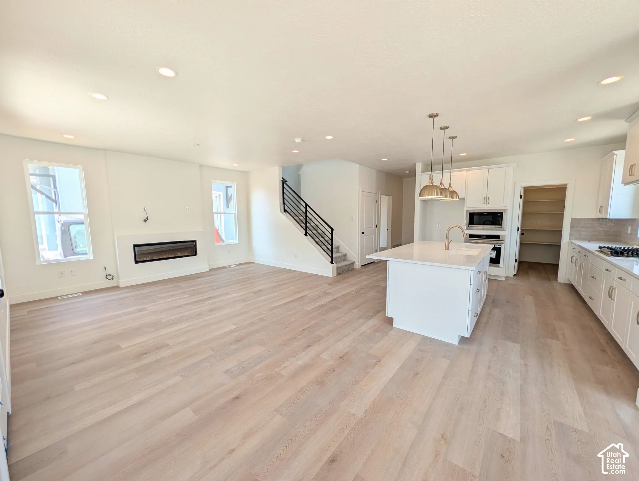 Open-concept living area featuring wood-finish flooring, a linear electric fireplace, and a kitchen island with a sink and pendant lighting