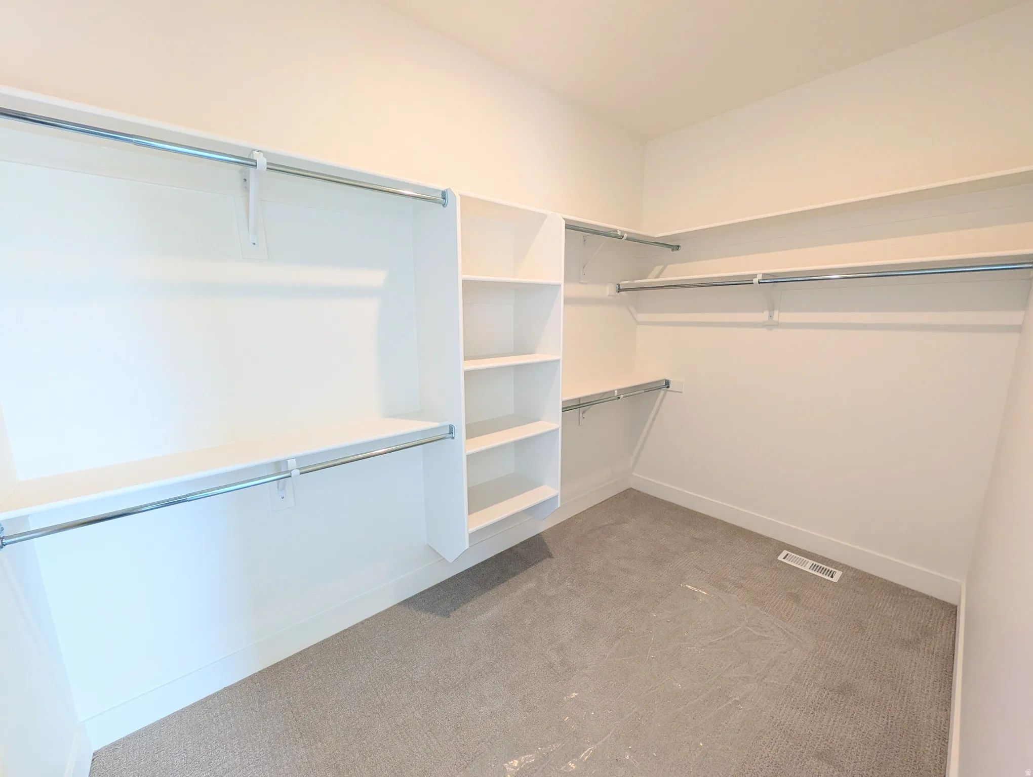 Expansive closet featuring integrated shelving, multiple hanging rods, and light-toned carpeting
