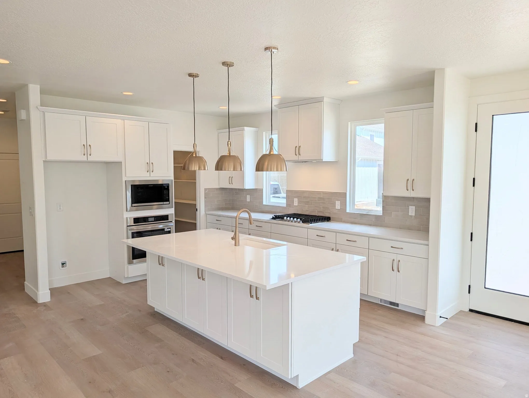 Kitchen featuring a large central island, white cabinetry, integrated stainless steel appliances, light wood-finish flooring, and pendant lighting