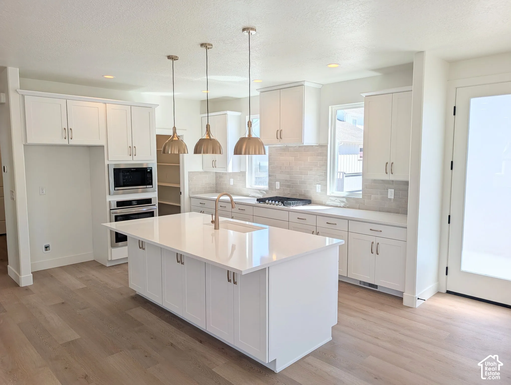 Kitchen featuring a substantial island with integrated sink, white cabinetry, integrated stainless steel appliances, and wood-finish flooring