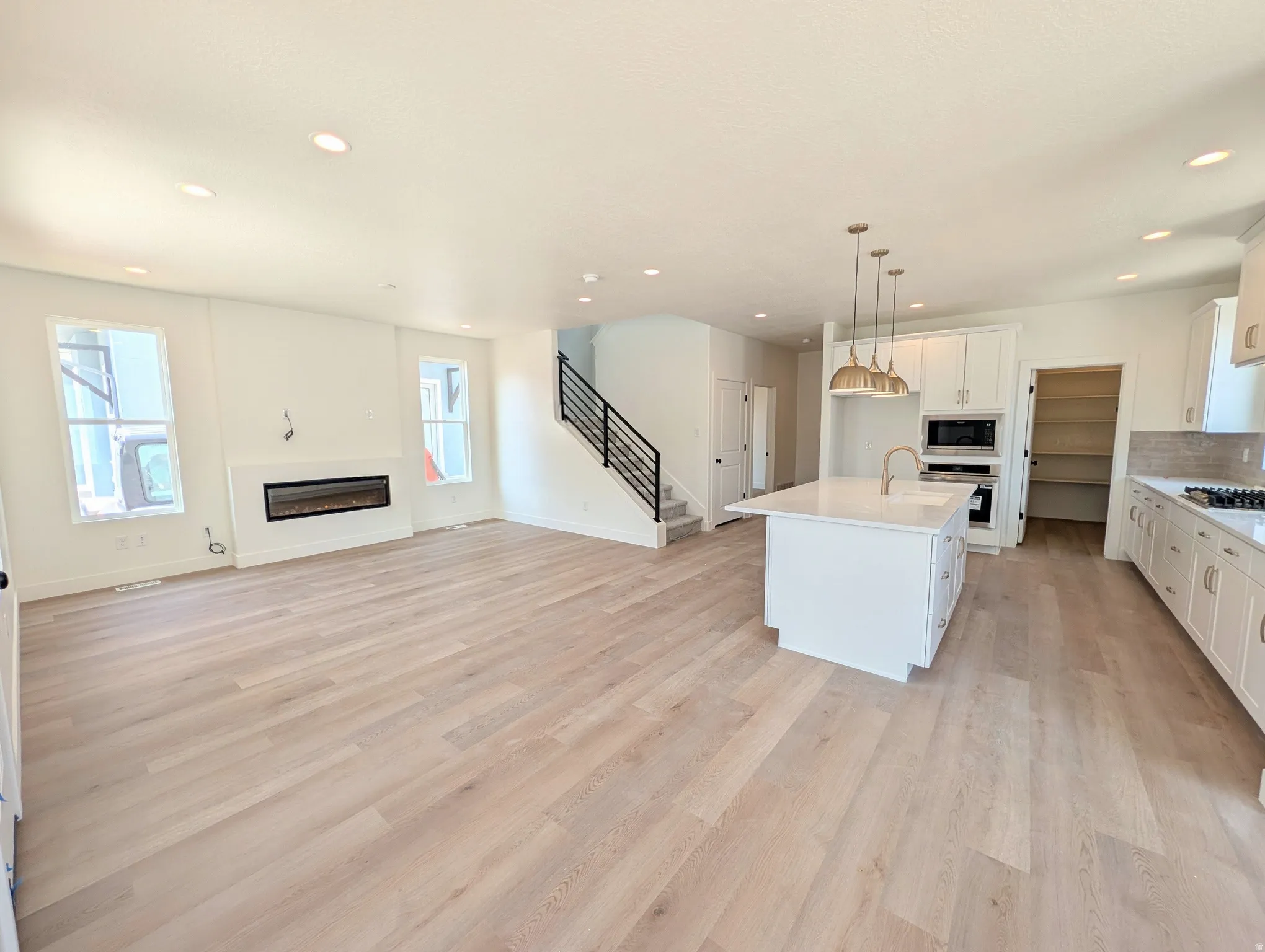 Open-concept living area featuring wood-finish flooring, a linear electric fireplace, and a kitchen island with a sink and pendant lighting
