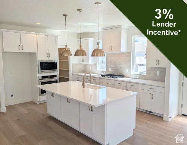 White shaker cabinetry with brass hardware, a central island with an undermount sink, built-in stainless steel appliances, and wood-finish flooring