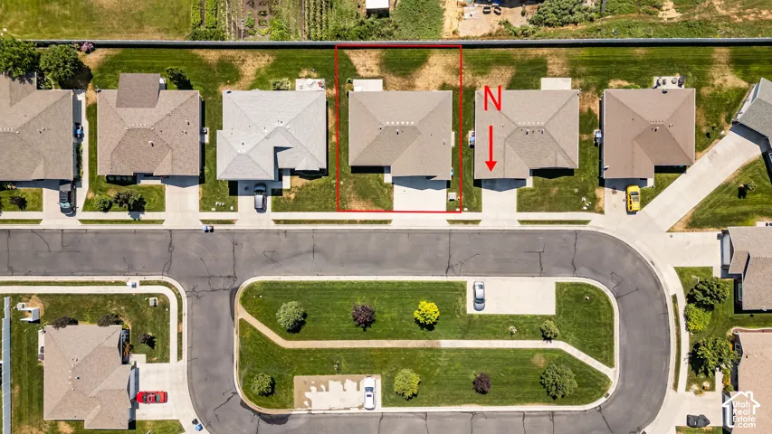 Aerial view of a residential property featuring a paved driveway, adjacent sidewalk, and a manicured lawn