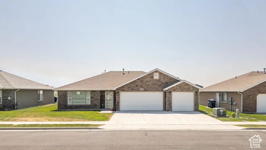 Brick facade with stone accents, dual attached garages, concrete driveway, and a front lawn