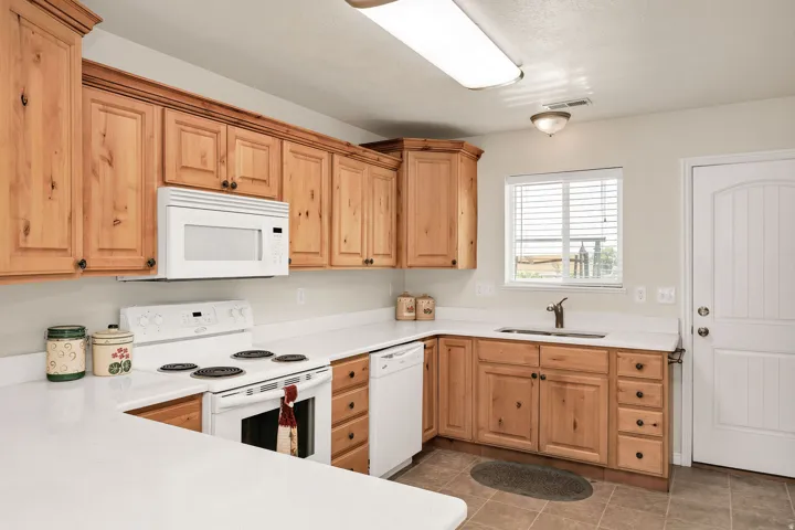 Wood cabinetry with dark hardware, white countertops and white applliances