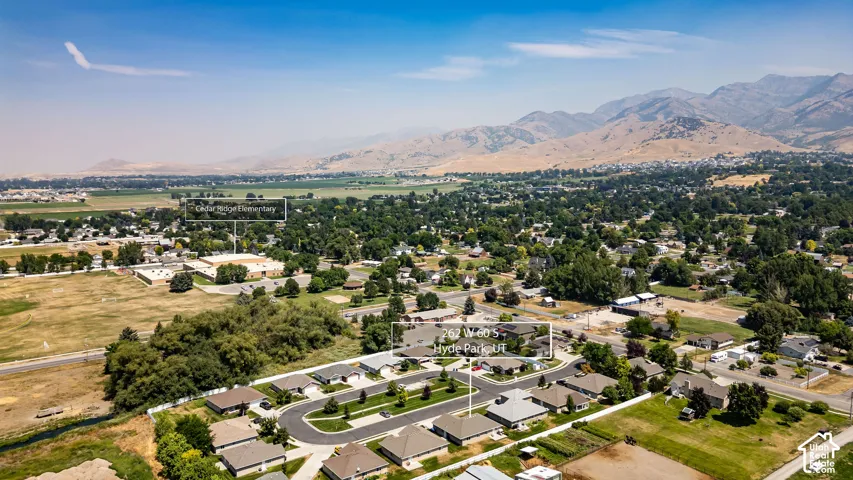 Aerial perspective showcasing a residential community with mature landscaping, an adjacent school, and distant mountainous terrain