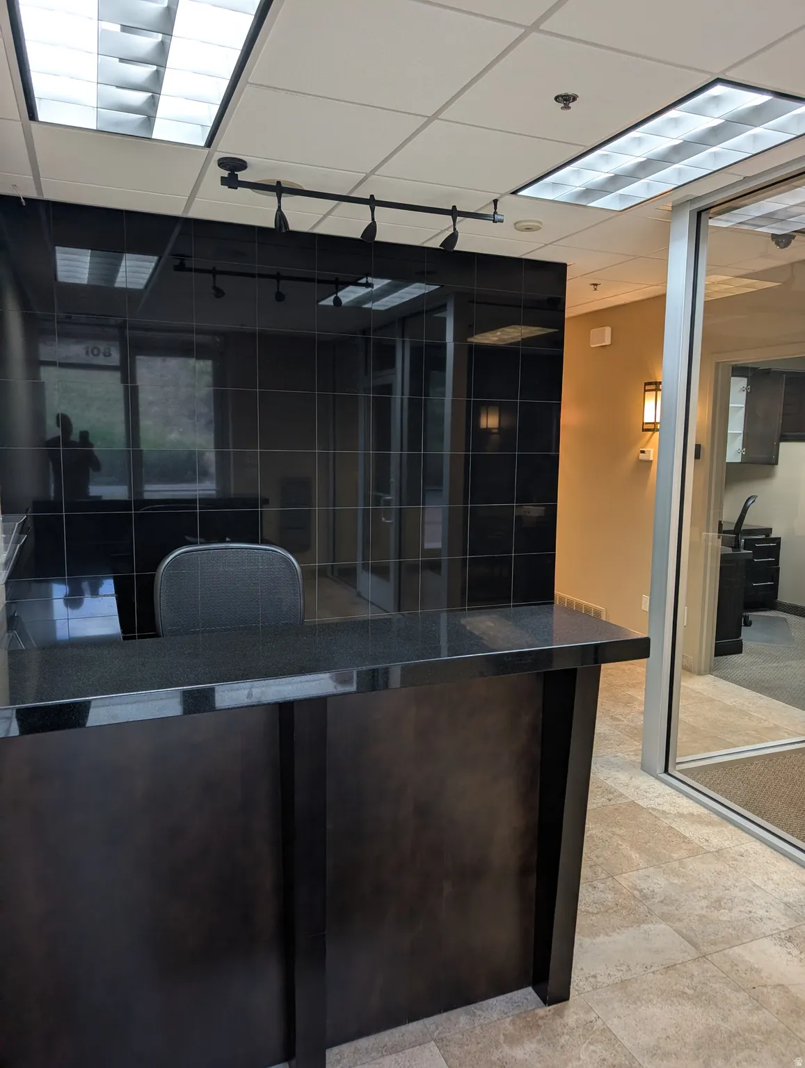 Reception counter with a dark countertop and paneled base, complemented by a tiled wall